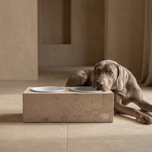Lade das Bild in den Galerie-Viewer, Grauer Hund liegt neben der beigen PRIGUR Cremó Futterstation mit zwei weißen Keramiknäpfen
