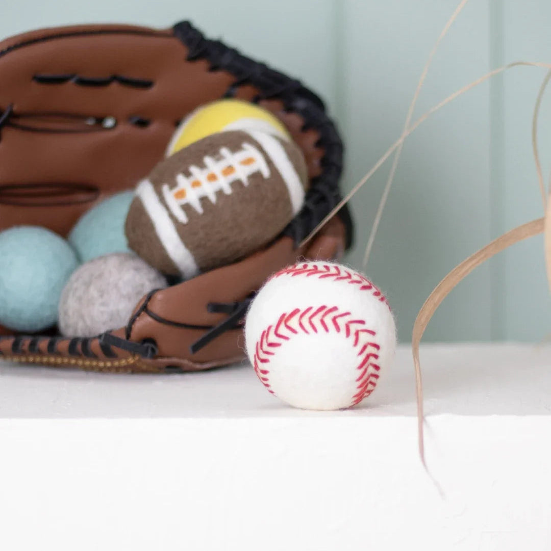BUDDY. Woll-Baseball vor einem Baseballhandschuh mit weiteren Filzbällen und einem Woll-Football
